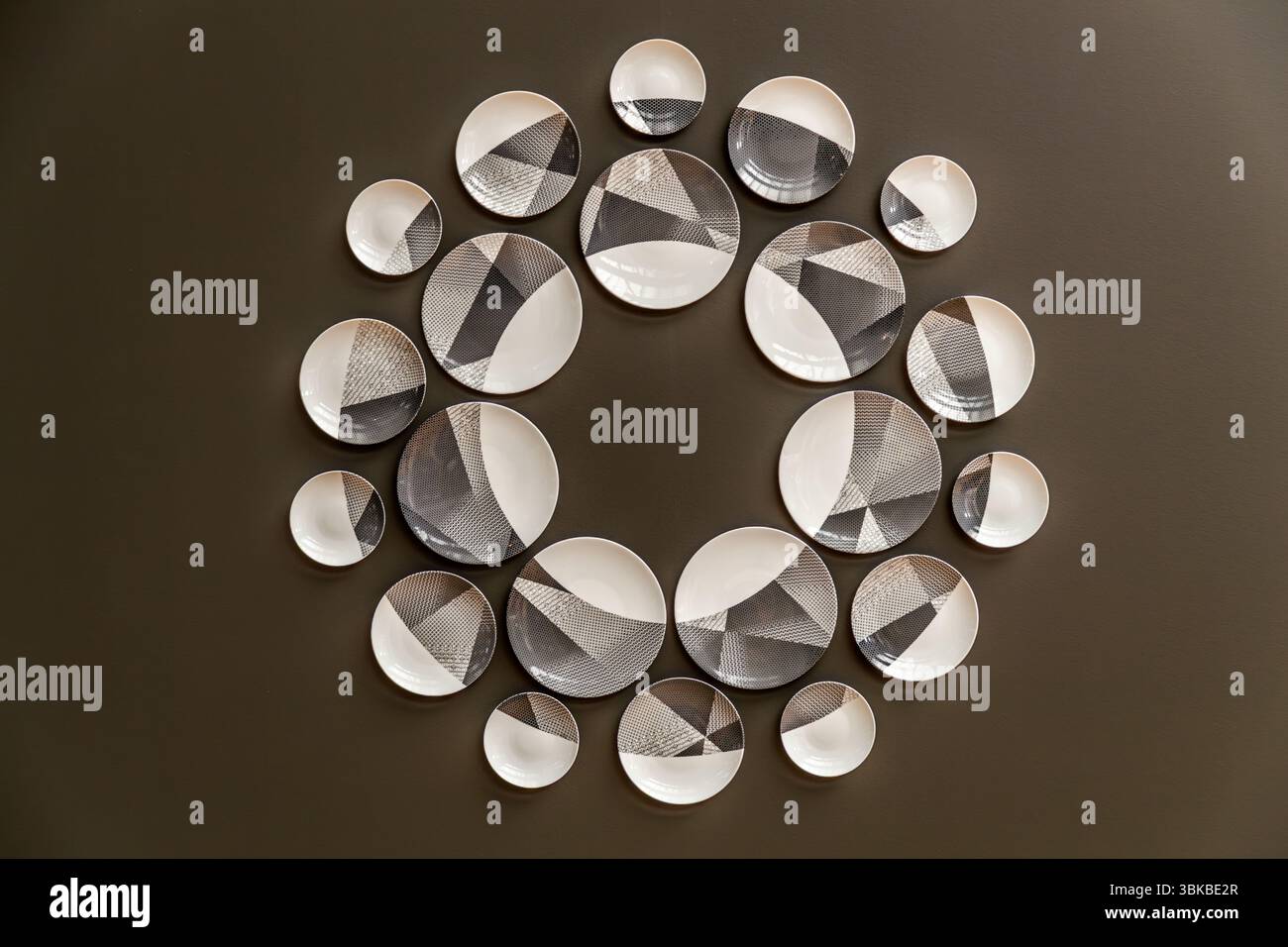 A modern porcelain series decorates a wall of the Musée National Adrien Dubouché on Place Winston Churchill in Limoges, Haute-Vienne, Nouvelle-Aquitaine, France. Around 20 white plates of various sizes hang in a circle on a dark brown wall. Their decoration consists of grey and black triangular areas with fine grid and dot patterns. The museum was founded in 1845 as the city's first museum. Adrien Dubouché, a patron of the arts and son of a cloth merchant, took over its management in 1865. He greatly expanded the exhibition through generous donations and the acquisition of important ceramic co Stock Photo