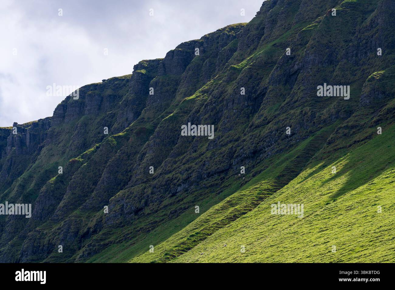 Steep rocky escarpment of Benbulben mountain with sunlit grassy slope ...