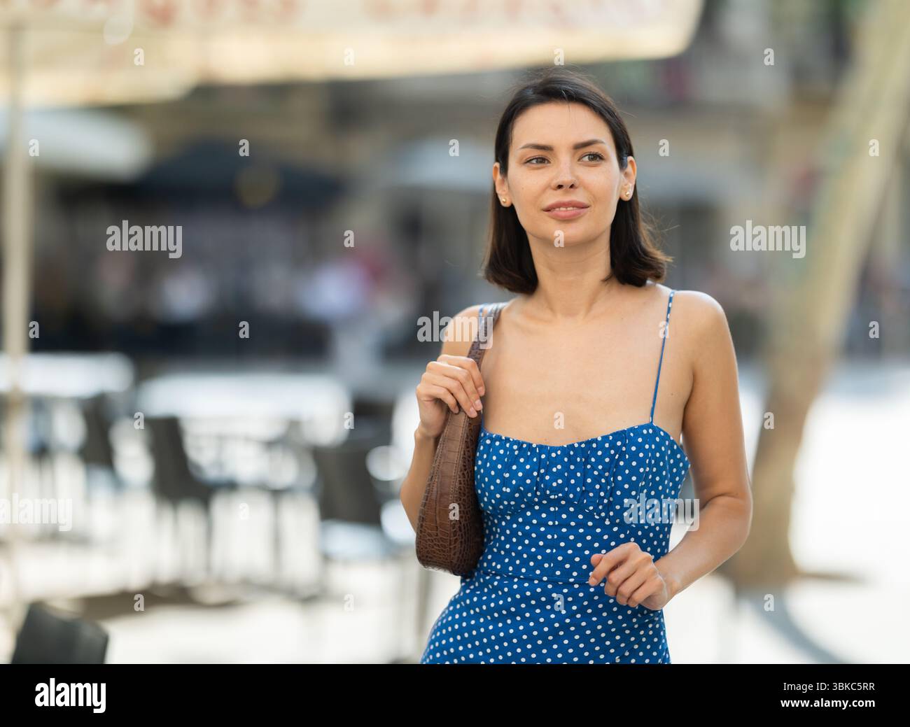Cheerful brunette girl in blue dress walking along the street among ...