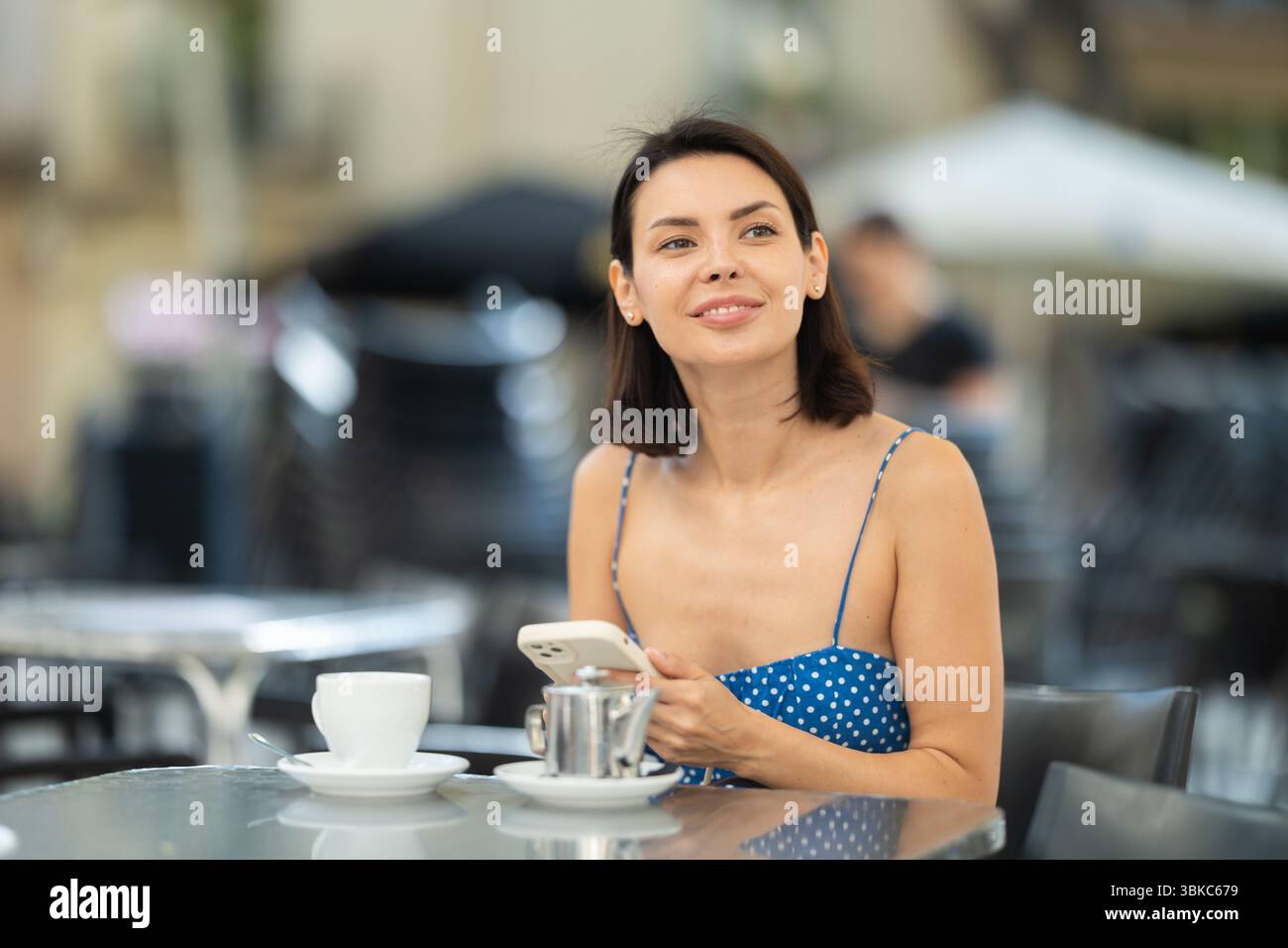 Brunette texting on smartphone screen during breakfast on cafe terrace. Drinking tea Stock Photo