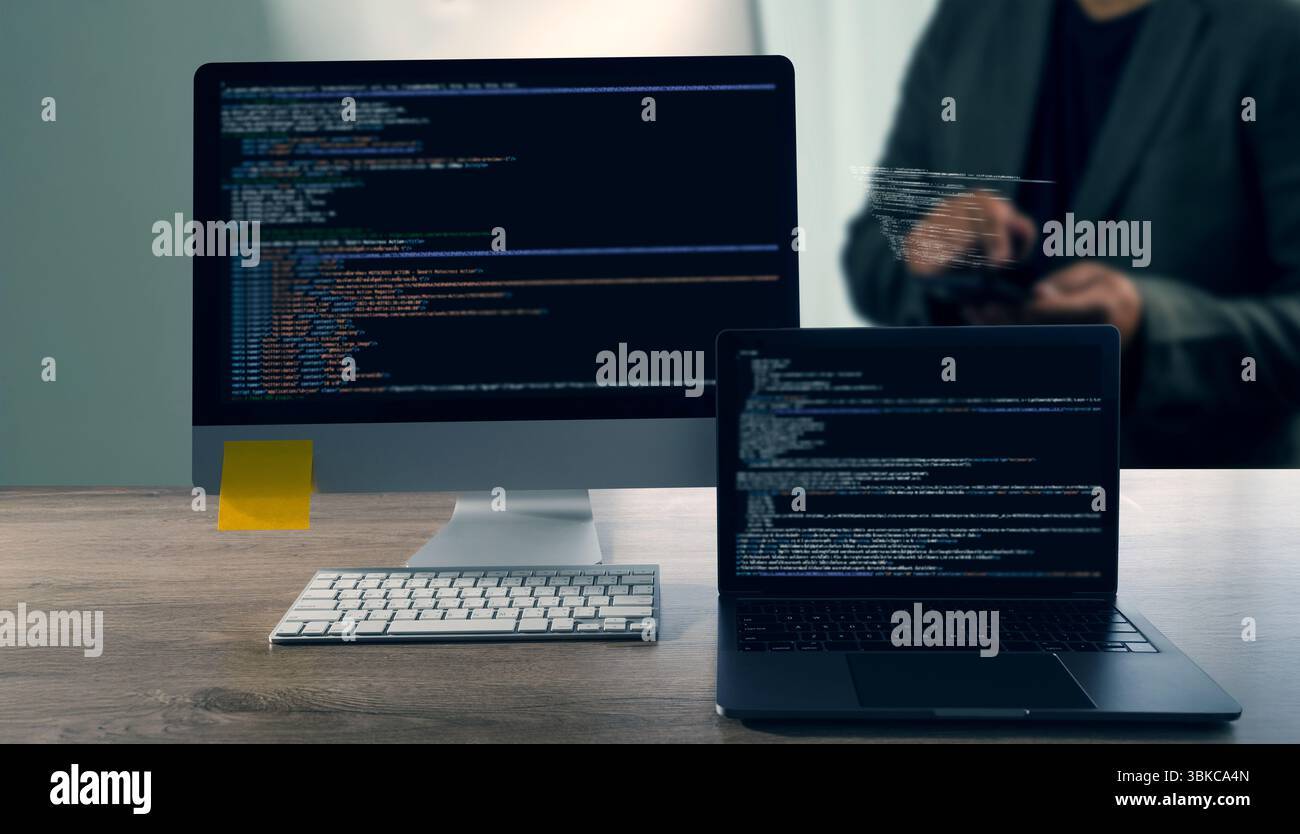 A programming code on representing close up of computer monitor and laptop displaying code, with person background using tablet, modern workspace Stock Photo
