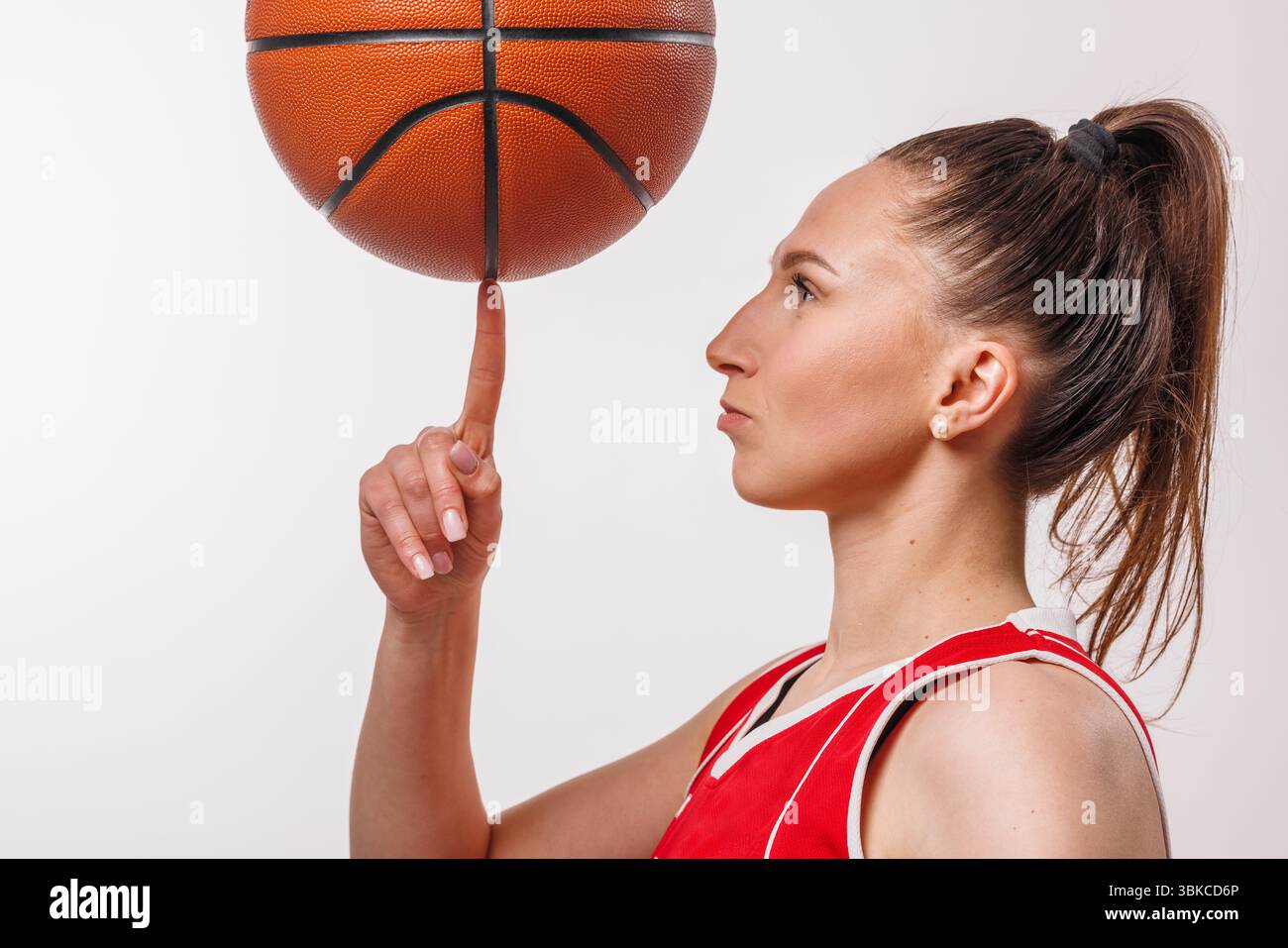 Skilled female basketball player in red jersey balancing ball on finger, symbolizing talent, focus, and athletic precision. Stock Photo