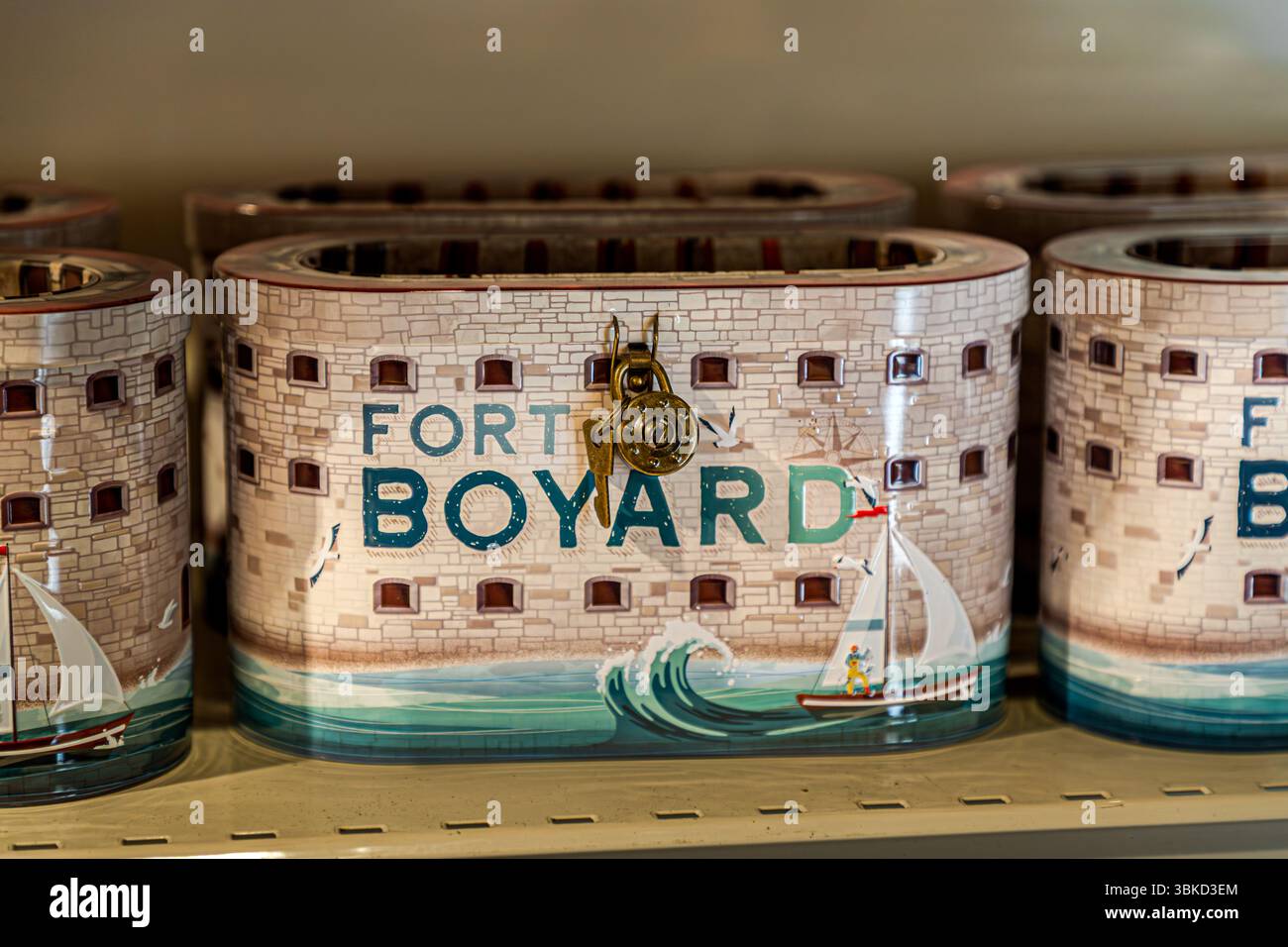 A tin money box in the shape of the famous Fort Boyard stands on a shelf in a shop on Rue Marengo on the island of Aix (Île d'Aix), Charente-Maritime, Nouvelle-Aquitaine, France. It bears the lettering "Fort Boyard", painted windows, a sailing boat and waves, and can be locked with a brass lock and key. The real fort is located on a sandbank between this island and the Île d'Oléron. It gained international fame through the adventure game show "Fort Boyard". The format was adapted in over 33 countries from 1990 onwards. It is considered the most successful French television export, with a huge  Stock Photo