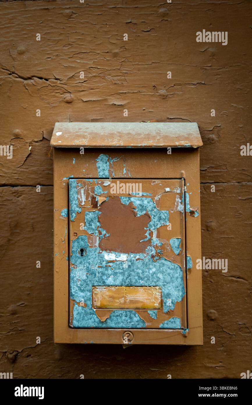 A rustic mailbox is mounted on a weathered brown wall, featuring peeling paint and faded colors. Auvergne. France Stock Photo