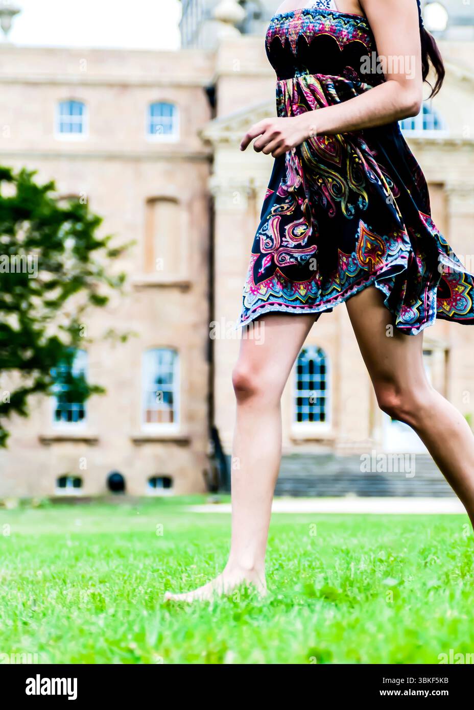 A woman in a colourful dress is running barefoot on the grass in front ...