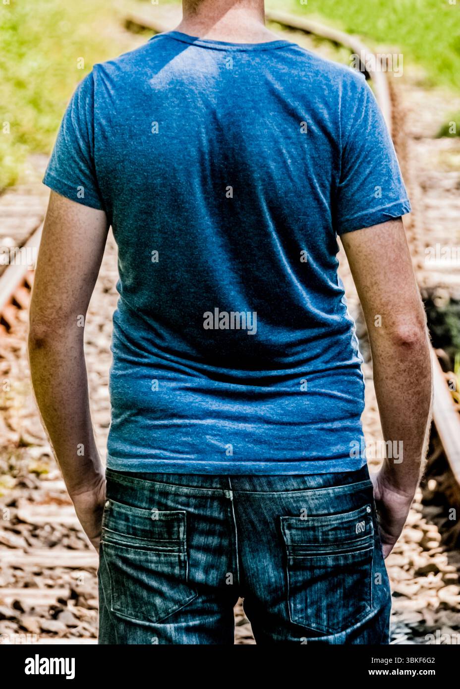 A man standing on train tracks, viewed from the back. Stock Photo