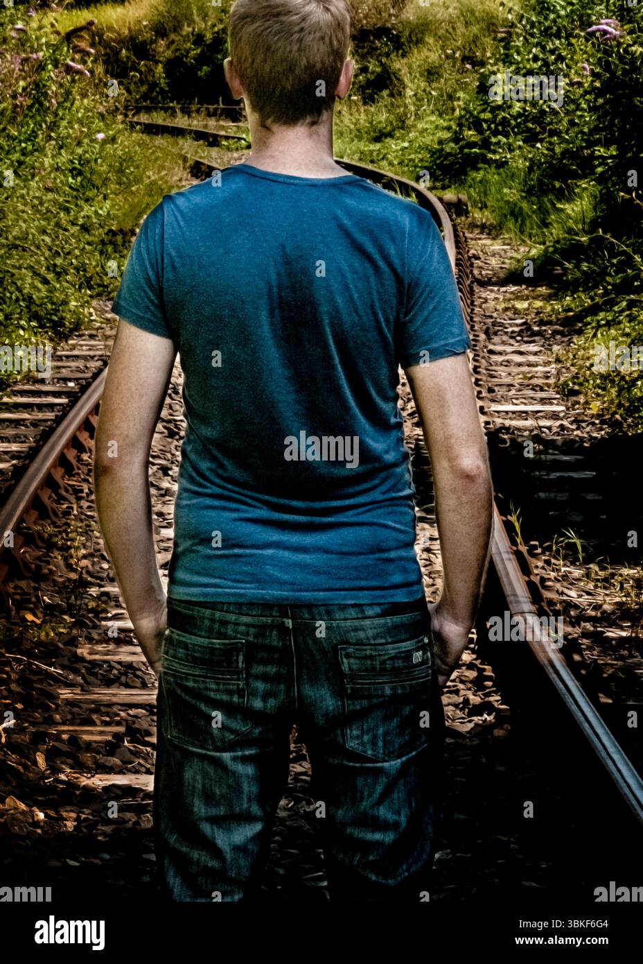 A man standing on train tracks, viewed from the back. Stock Photo
