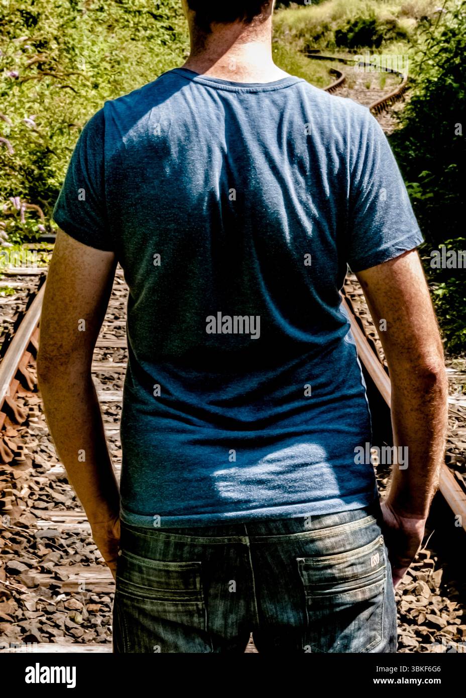 A man standing on train tracks, viewed from the back. Stock Photo