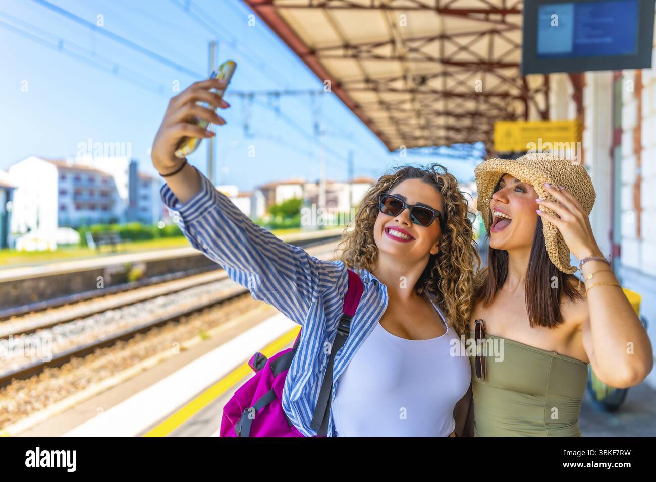 Two happy female tourists taking a selfie with a smartphone at a train station before departure Stock Photo