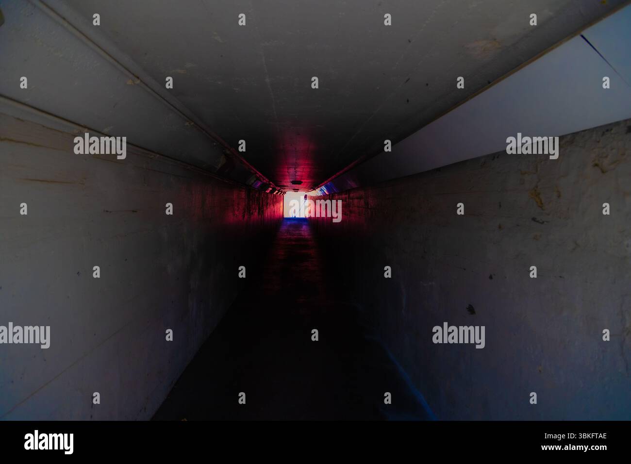 Long dark empty tunnel walkway with light at the end. Stock Photo