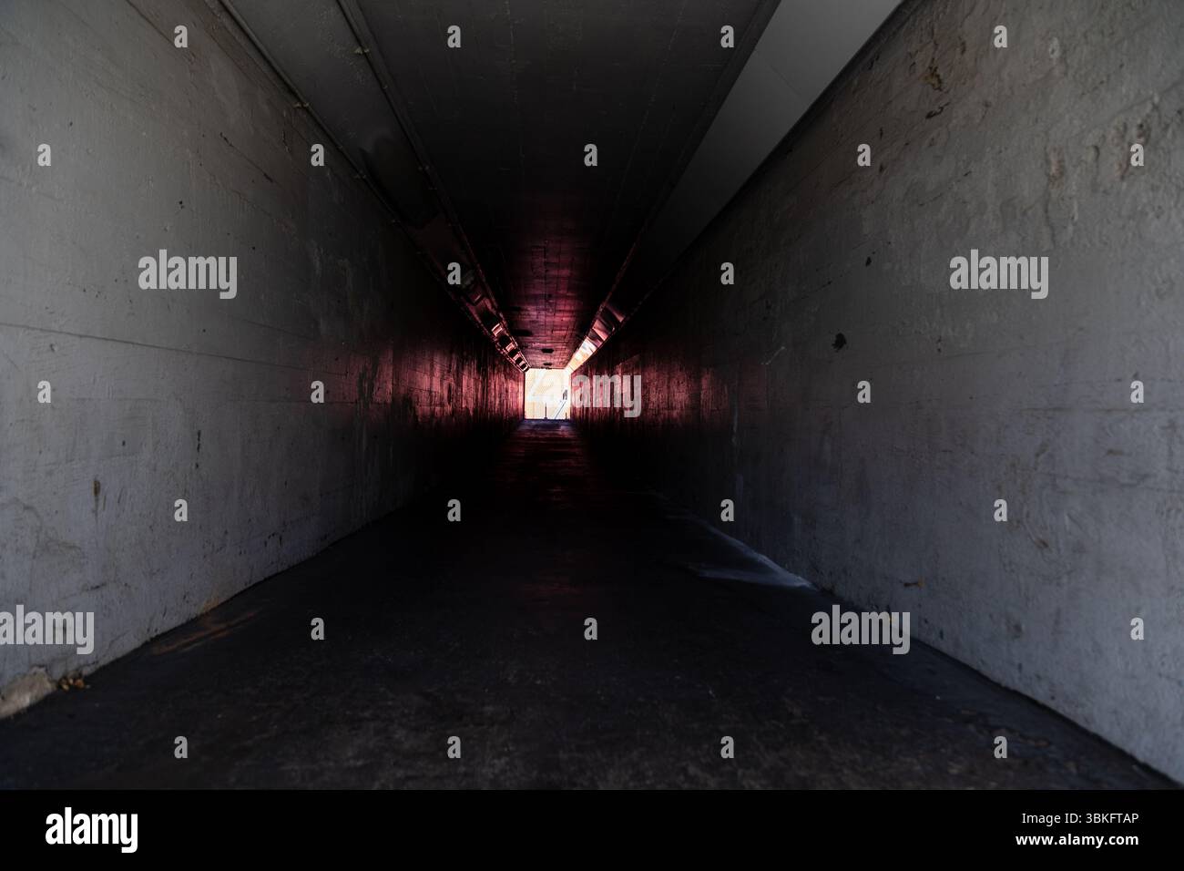 Long dark empty tunnel walkway with light at the end. Stock Photo