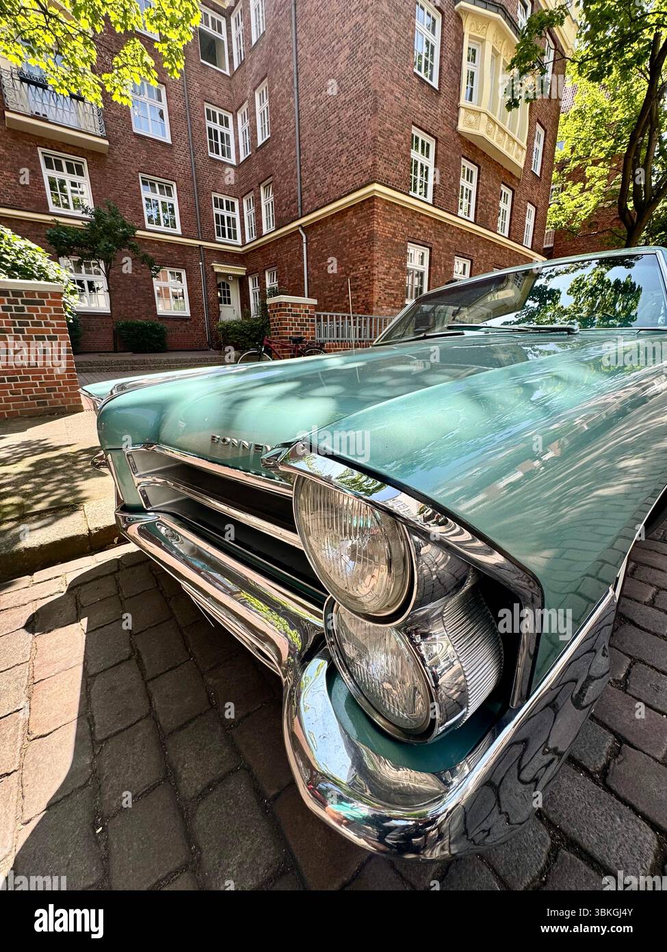close-up shot of a classic turquoise Pontiac car parked in front of historic red-brick residential building on a sunny day in Hamburg, germany. - Smartphone Captured Stock Image