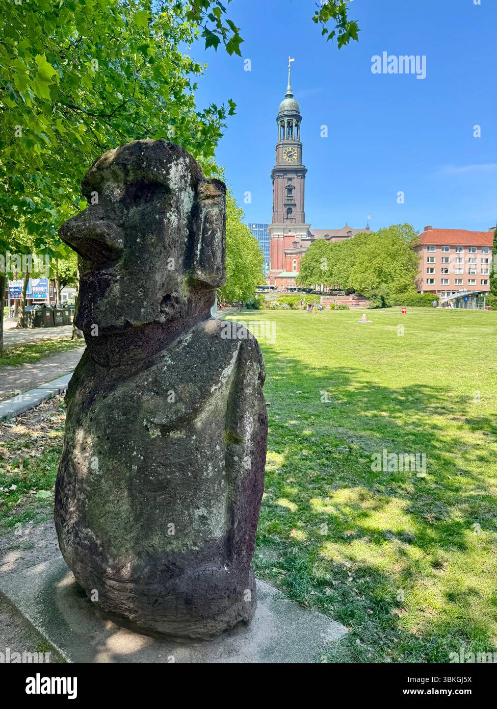 Stone sculpture resembling a Moai statue with St. Michael's Church (Michel) in the background, Hamburg, Germany. - Smartphone Captured Stock Image