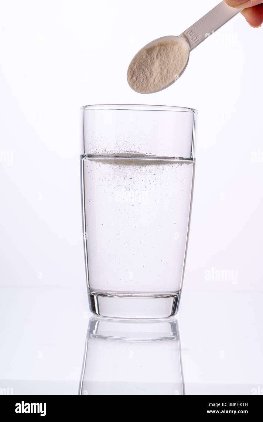 Collagen powder is poured with a measuring spoon into a glass of water on a white background with a reflection. The medicine is diluted in water. Vert Stock Photo