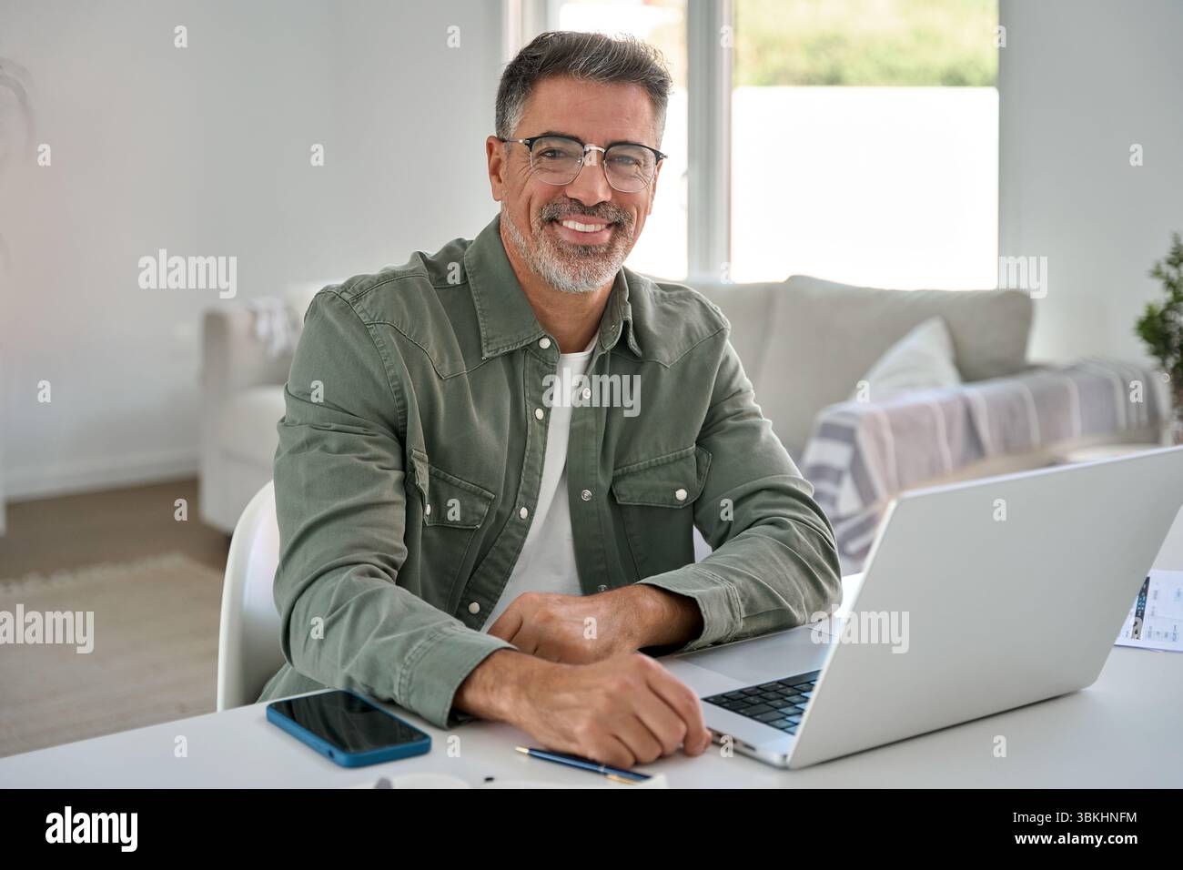 Happy middle aged man using laptop computer at home table. Portrait Stock Photo