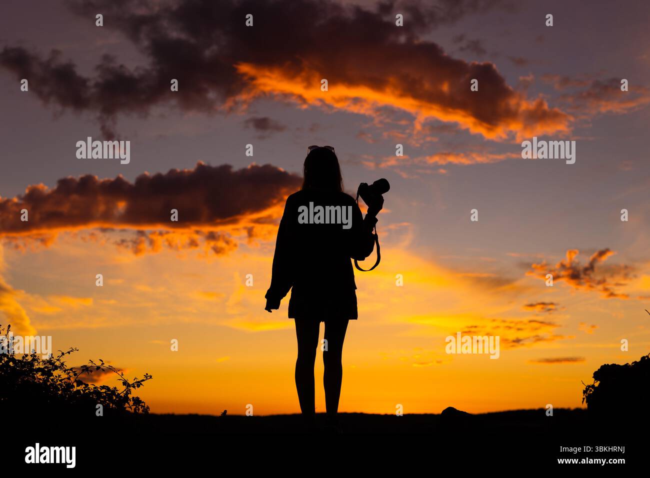 Silhouette of woman with camera against sunset sky Stock Photo