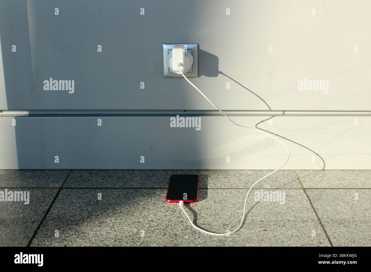a red iPhone charging from a wall socket with EU adapter from british plug Stock Photo