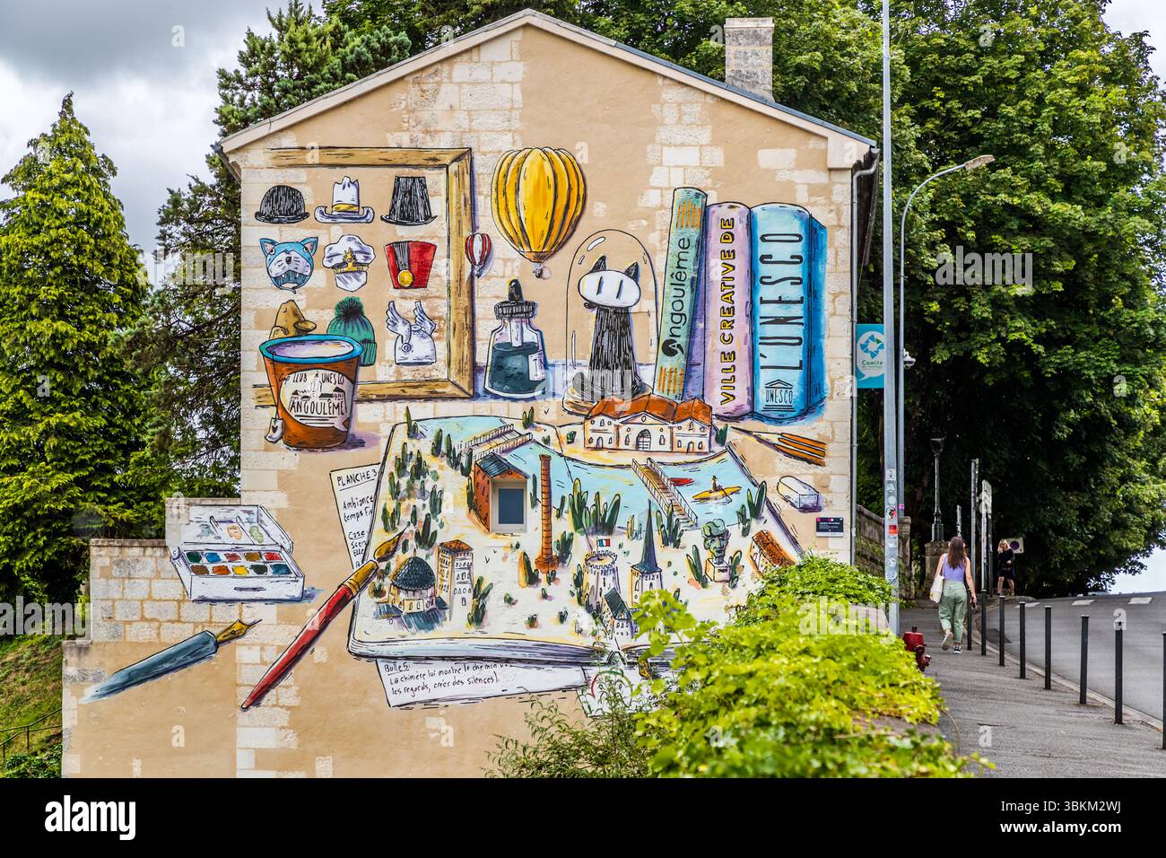 The newest mural on Avenue de Cognac in Angoulême, Nouvelle-Aquitaine, France (as of June 2025), celebrates the city's status as a UNESCO Creative City. Its elements represent the city's culture and history. The artwork combines comics, architecture and the local landscape into a colourful manifesto. It celebrates local creativity and cultural richness. An open sketchbook on the gable shows a drawn townscape with towers, a factory chimney and a river with a kayaker. Next to it stand books titled "Angoulême" and "Ville créative de l'UNESCO", a hot-air balloon, a cat under a glass dome and an in Stock Photo