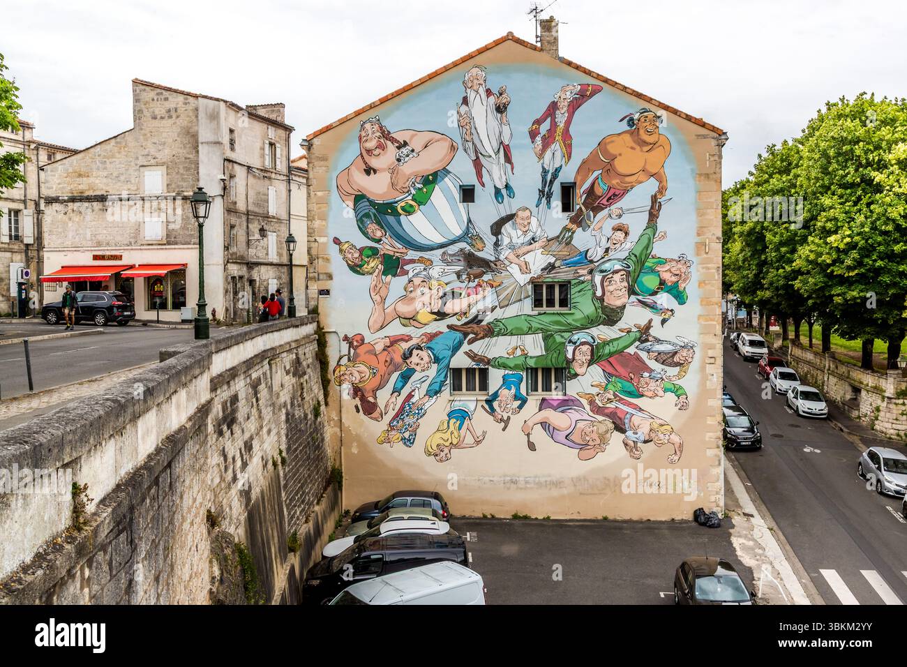 The mural Der Kosmos von Uderzo (The Cosmos of Uderzo) by François Boucq shows Albert Uderzo, the illustrator of Asterix and co-creator (together with René Goscinny) of the world's most famous Gauls, at his drawing table. The characters that have shaped generations of readers literally explode from the tabletop – a perfect metaphor for the artist's creative power. Mural in the Rue Léonard Jarraud in Angoulême, France. It shows a variety of comic characters, including Asterix and Obelix, depicted in a dynamic scene. The artwork is part of the city's famous comic strip murals, which celebrate An Stock Photo