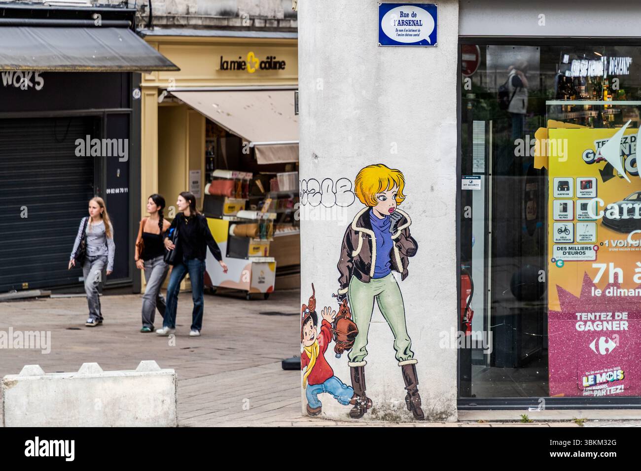 The mural of Natacha and the P'tit Bout d'chique on the corner of Rue de l'Arsenal and Rue Hergé in Angoulême, Nouvelle-Aquitaine, France, was the city's first wall comic. Flight attendant Natacha travels around the world in Belgian cartoonist François Walthéry's comic series and has been shaping the role model of a self-confident woman since 1970. She wears a flying jacket with a fur collar, while the little boy in a pilot's cap and yellow scarf reaches for her bag. The mural dates from 1999. The speech-bubble street sign explains the name of Rue de l'Arsenal: a building of the former counts' Stock Photo