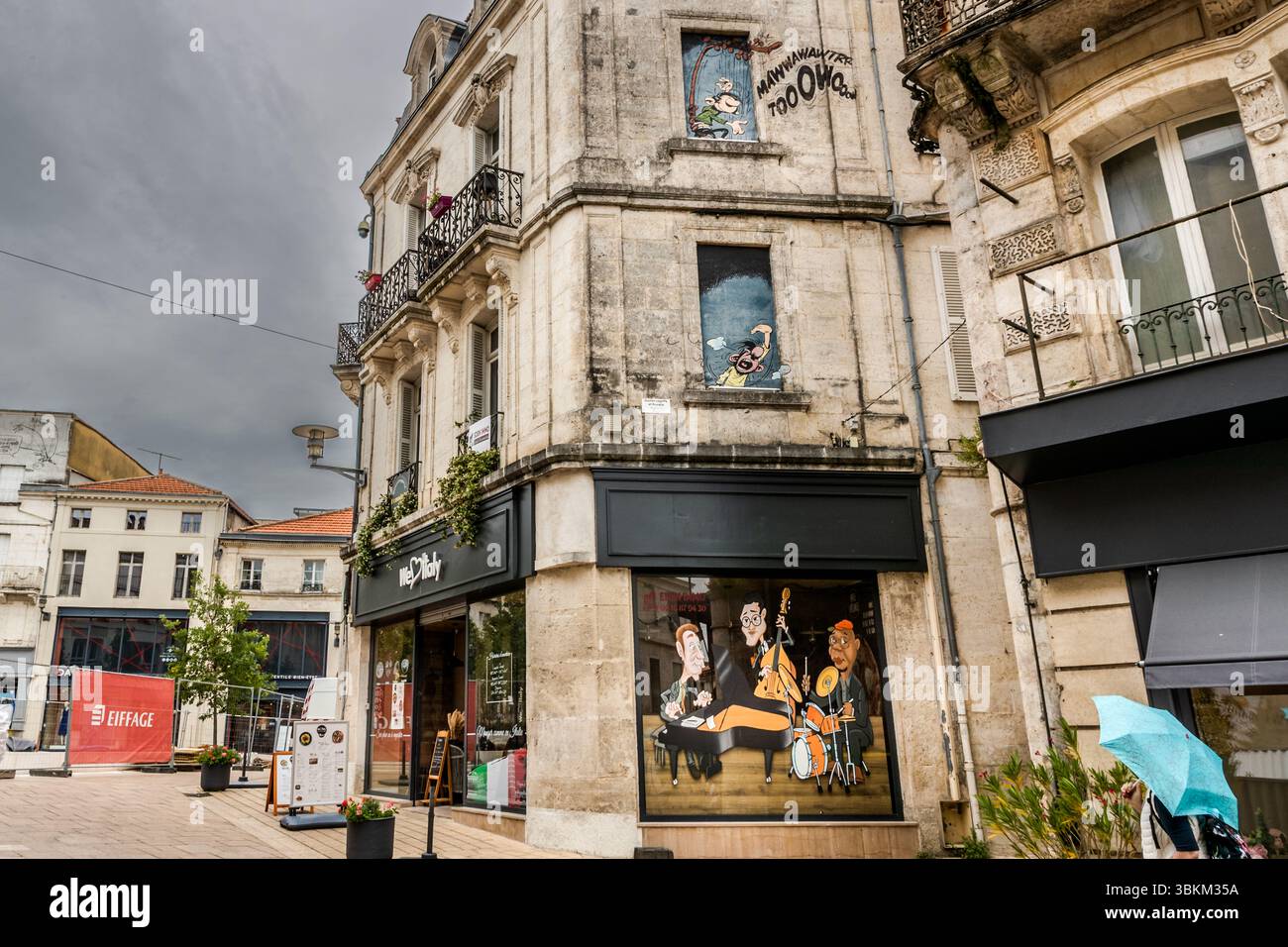 André Franquin's chaos duo on a corner building: Gaston plays the gaffophone in the upper window, while office manager Prunelle roars from the window below, red with rage, Rue Hergé, Angoulême, Nouvelle-Aquitaine, France. Gaston and Prunelle are characters from the Belgian comic strip created by André Franquin. Gaston's original name is "Gaston Lagaffe", a chaotic office messenger who causes many mishaps. Prunelle's original name is "Léon Prunelle", and he is Gaston's choleric office manager. The gaffophone is a type of harp that makes absolutely unpleasant noises, at least according to Prunel Stock Photo