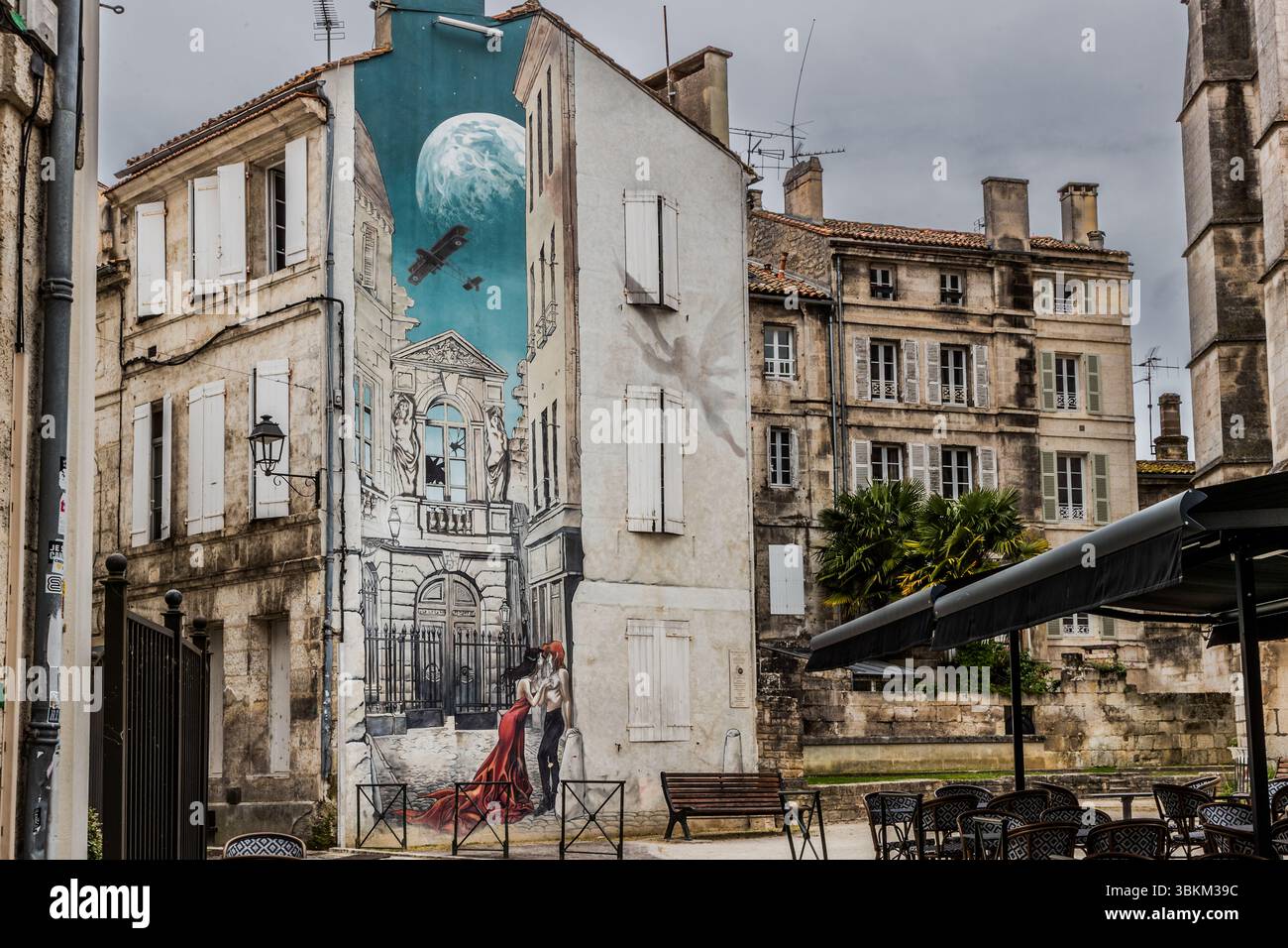 A mural depicts a scene with a couple, an aeroplane and a moon set against the backdrop of historic architecture. It is an example of street art that beautifies the city and reflects the history and culture of the region. Angoulême is recognized as a UNESCO Creative City in the category of literature since 2019. Rue Sainte-Marie, Angoulême, Nouvelle-Aquitaine, France Stock Photo
