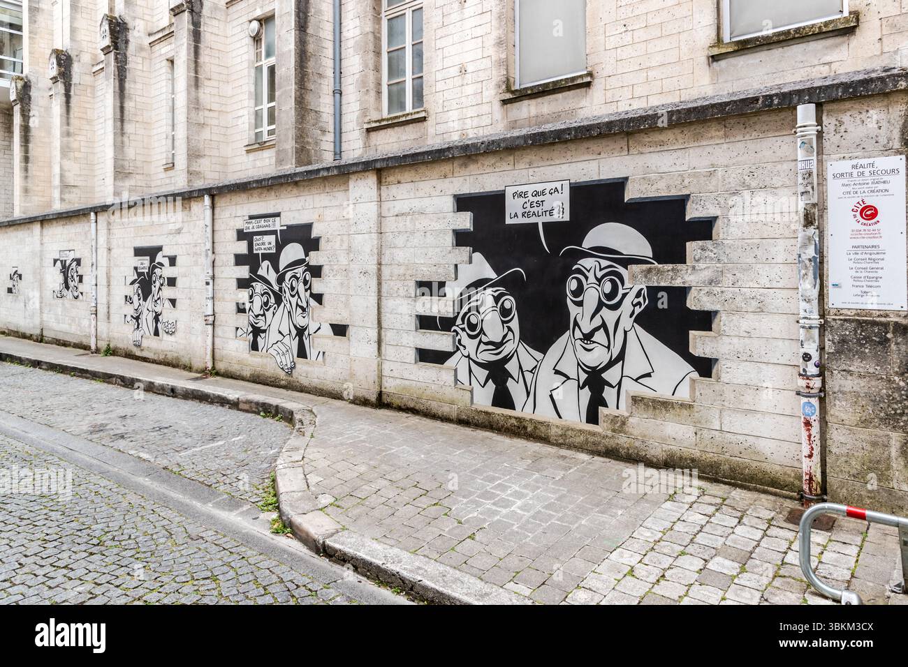 Marc-Antoine Mathieu's "Réalité, Sortie de Secours" (Reality, Emergency Exit) is a meta-comic on the wall that lets comic characters break out of it, Rue de Beaulieu, Angoulême, Nouvelle-Aquitaine, France. The mural depicts comic book characters with speech bubbles that appear to be bursting out of the wall. In six panels along the wall, the series tells a complete story: "Do you see anything? Yes, look. It's exactly what I feared. What, another underworld? Worse than that. It's reality." In the largest panel, two men in hats and round glasses say "Pire que ça! C'est la réalité!" In English: ' Stock Photo