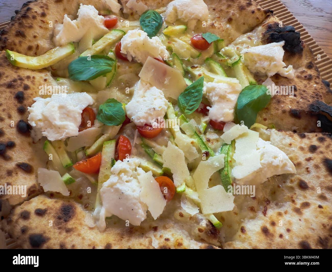 A hot pizza is topped with mozzarella, cherry tomatoes, zucchini, and fresh basil, showcasing a perfect blend of flavors. - Smartphone Captured Stock Image