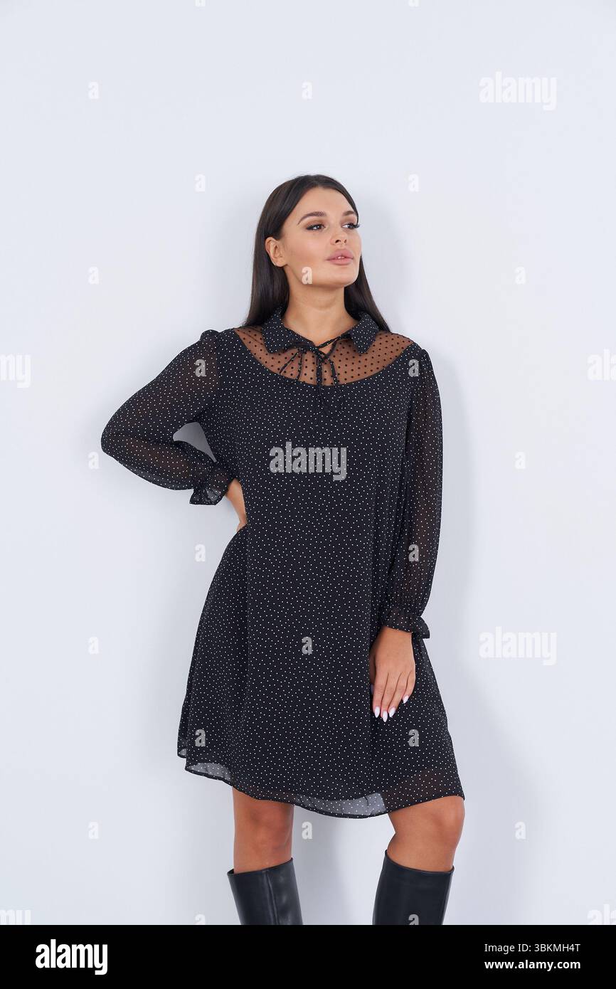 Woman with long dark hair wearing a black polka dot dress stands ...