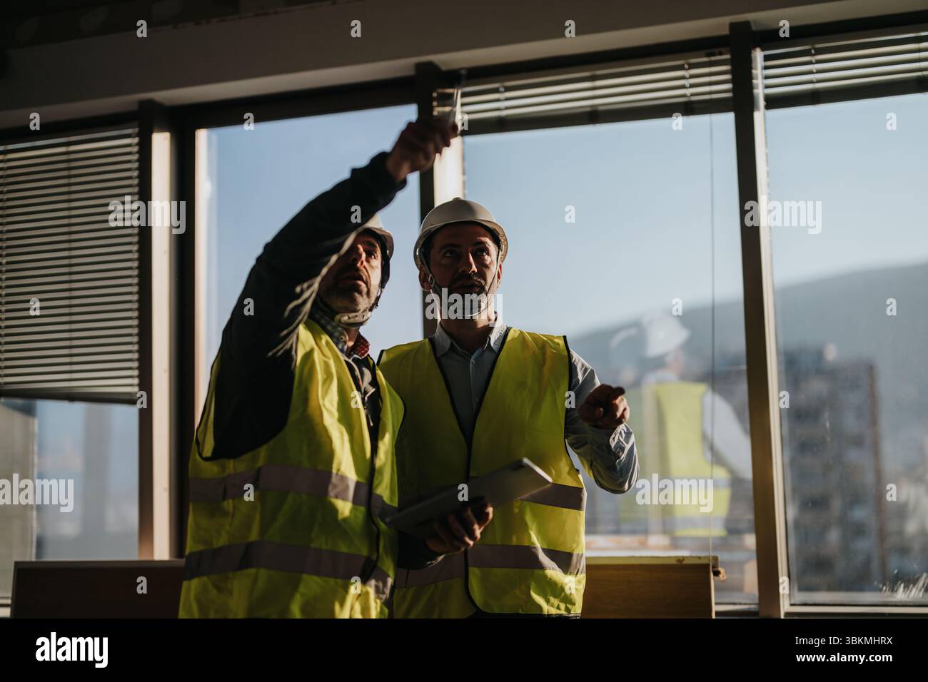 Construction professionals collaborating inside a building during daylight hours, inspecting architectural plans and discussing project progress. Stock Photo