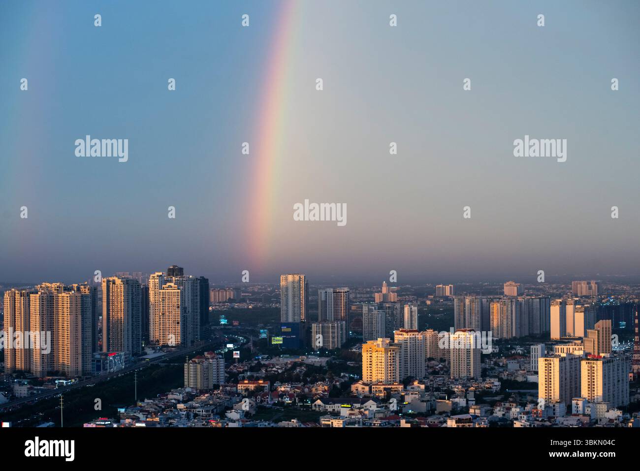 Rainbow is seen in the sky above a city. The rainbow is long and spans from the left side of the image to the right side Stock Photo