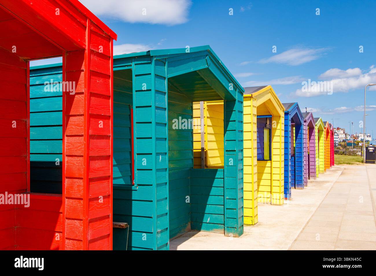 A vibrant row of colourful beach huts painted in bright red, green, yellow, blue colors & sunny blue sky along seaside , seaton carew, co. durham uk Stock Photo