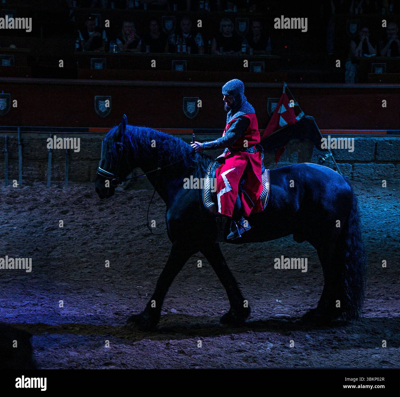 A medieval knight dressed in red armor rides a black horse in a dimly ...