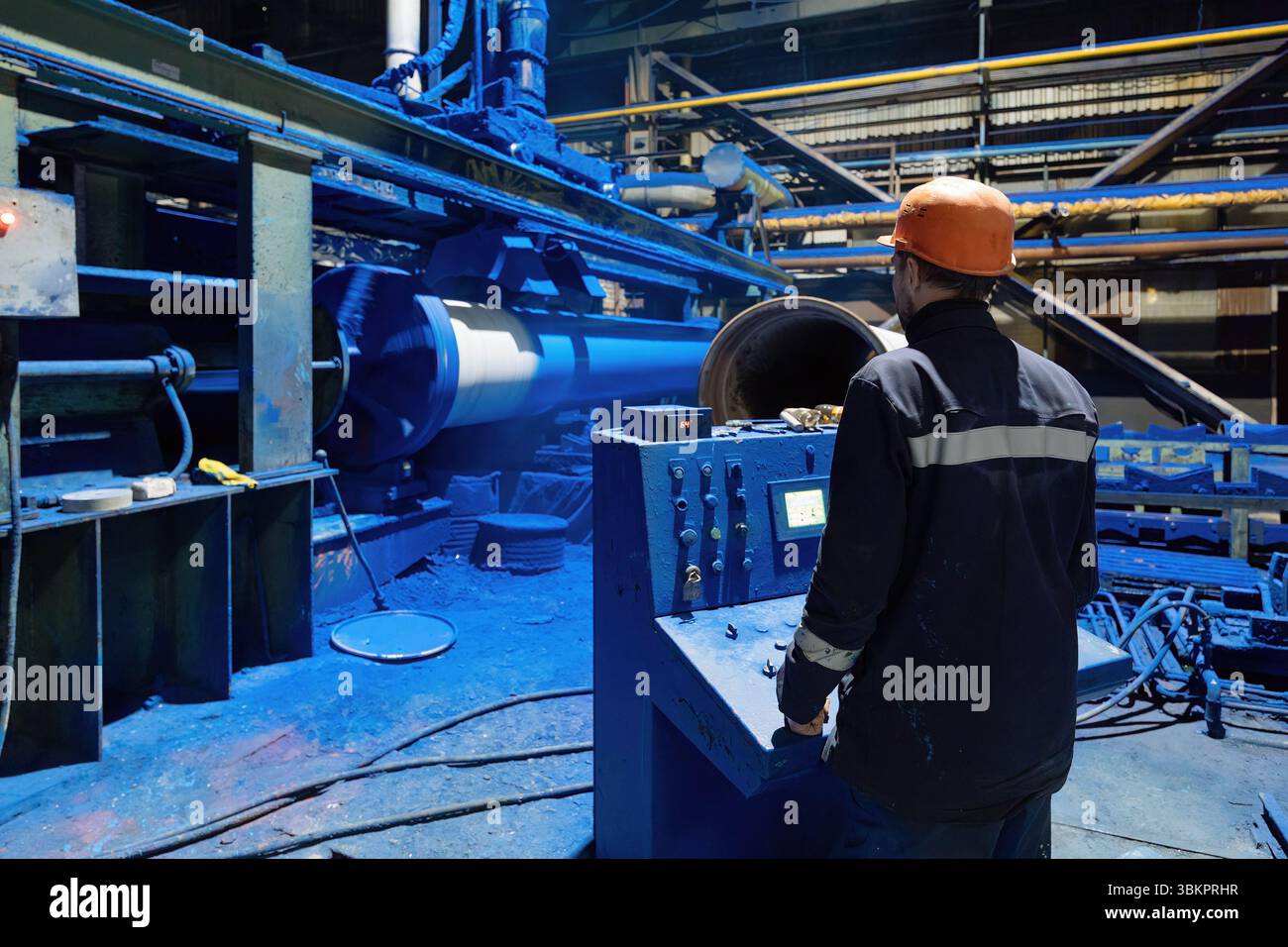 Factory engineer operates pipe painting automatic machine. Stock Photo