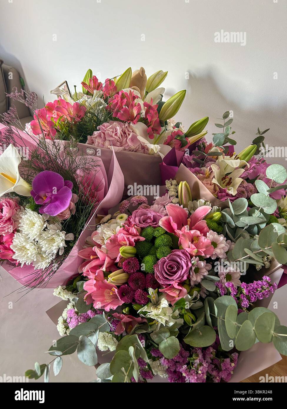 A vibrant collection of flower bouquets featuring lilies, roses, orchids, chrysanthemums, and eucalyptus, arranged in soft pastel wrapping paper. - Smartphone Captured Stock Image