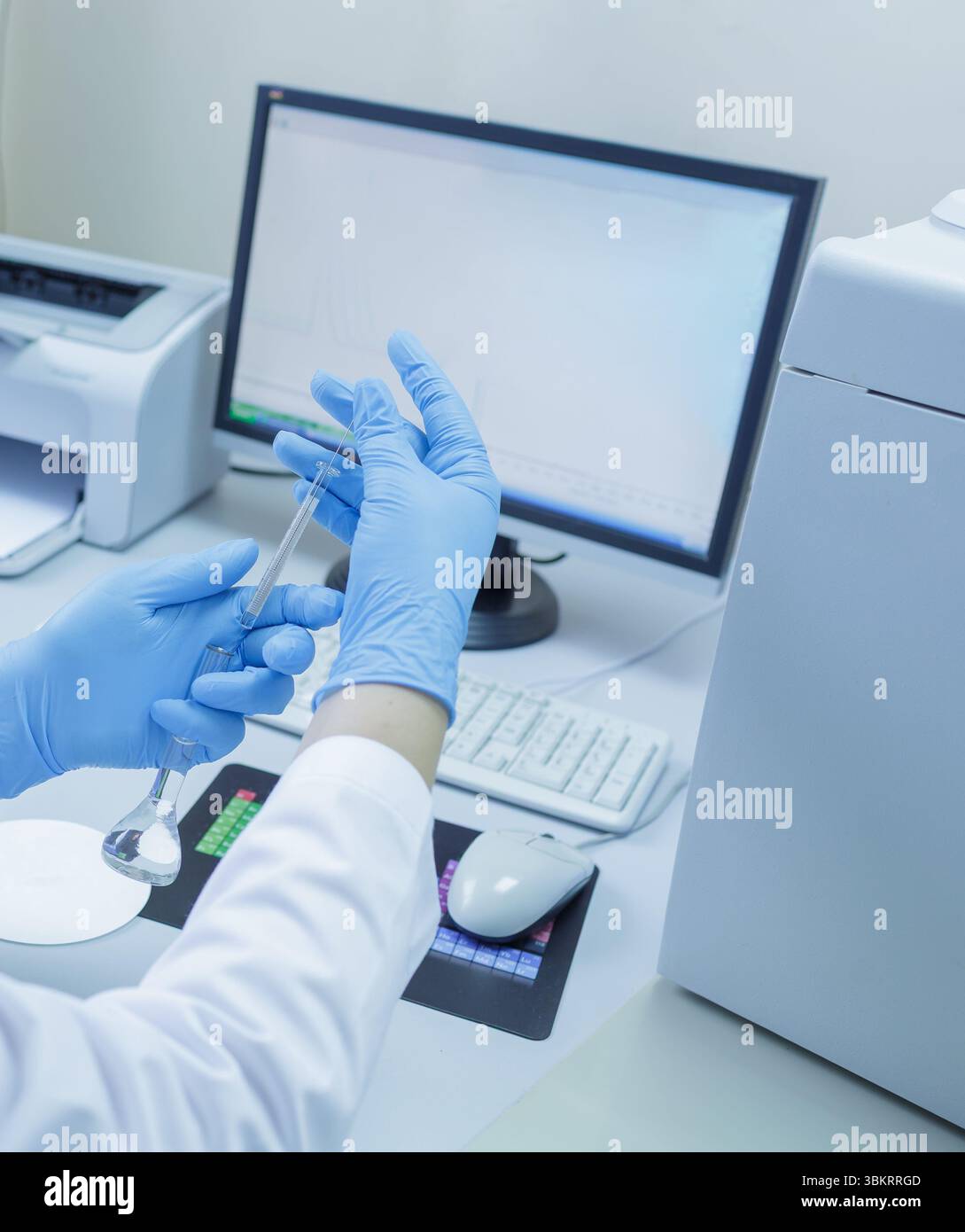 Lab technician in gloves analyzing samples with scientific glassware and computer in a modern medical laboratory Stock Photo