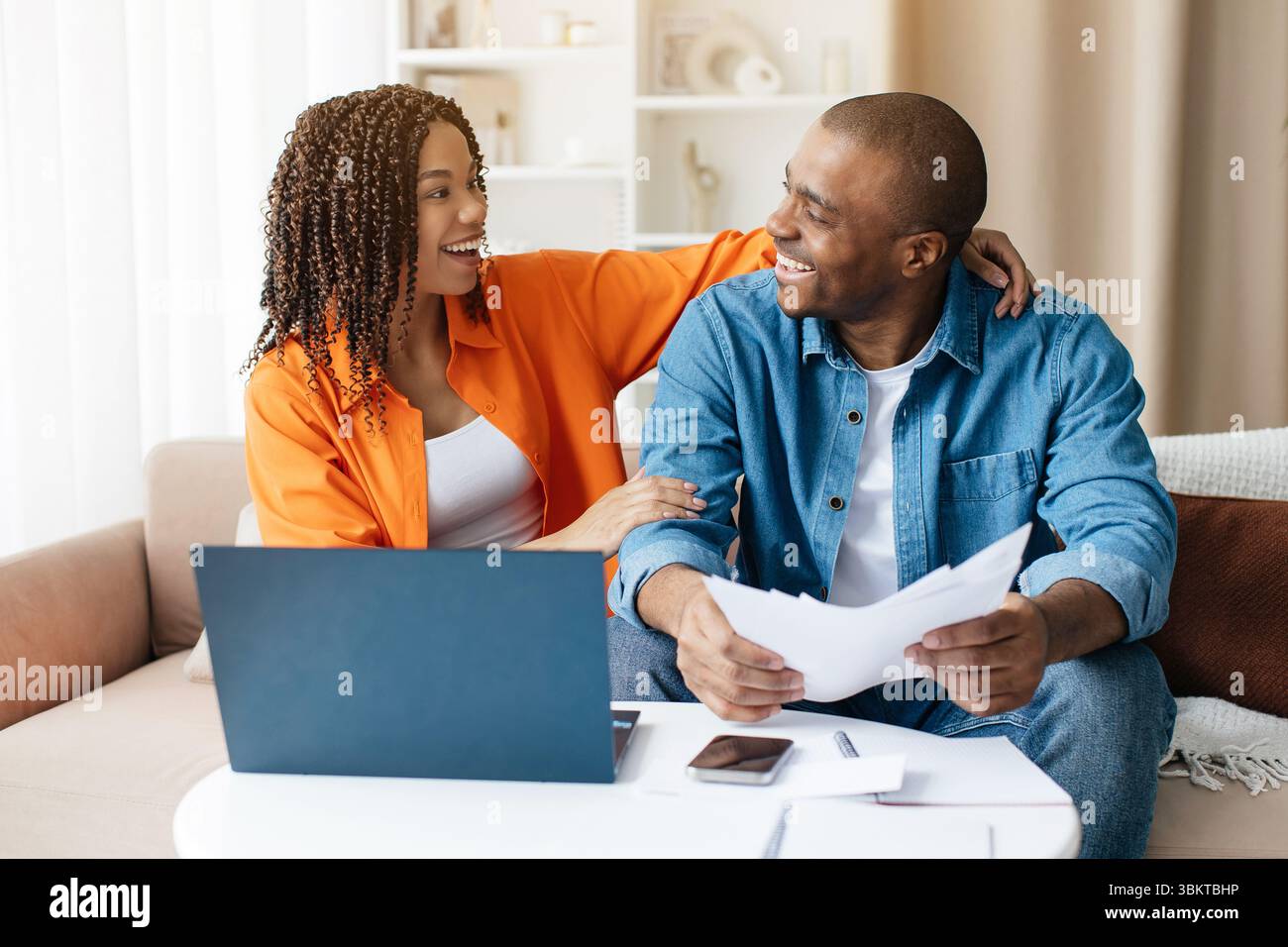 Happy African American couple smiling while reading financial papers at home Stock Photo