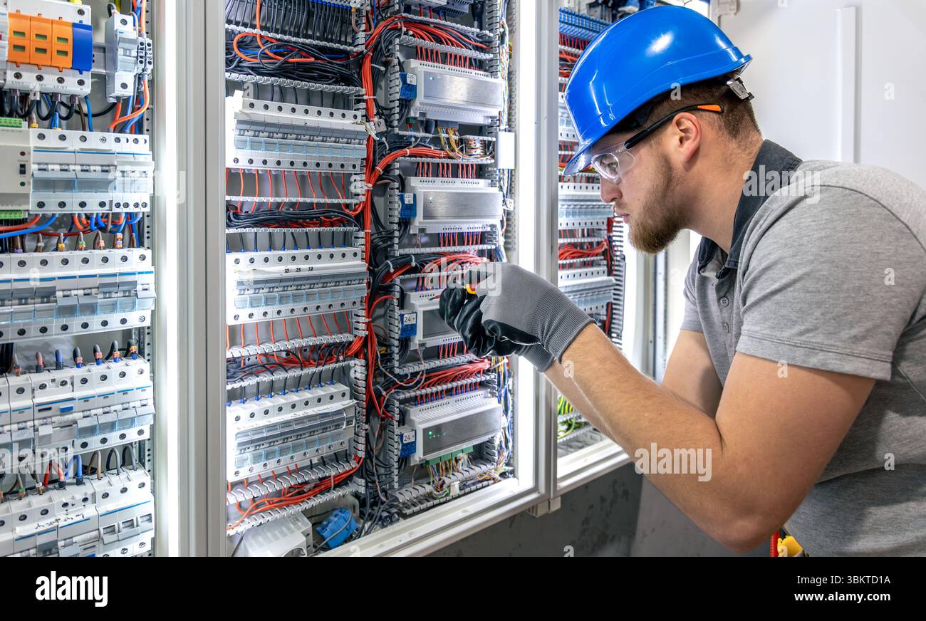 Electrician working in switchboard. Electrical component setup. Cable connection. Stock Photo