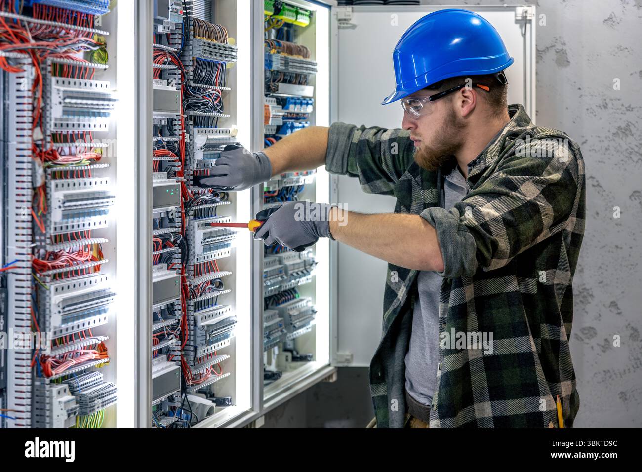 Electrician inspects connection. Working inside switchboard. Tool in hand. Stock Photo