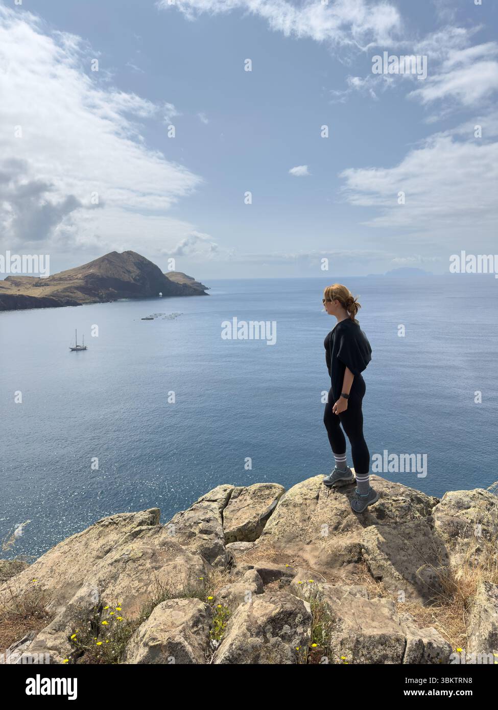 Tourist stands on edge of cliff on rocky coast of Ponta de Sao Lourenco Madeira Island, surrounded by waves and huge rocks, freedom and wind. Vertical - Smartphone Captured Stock Image