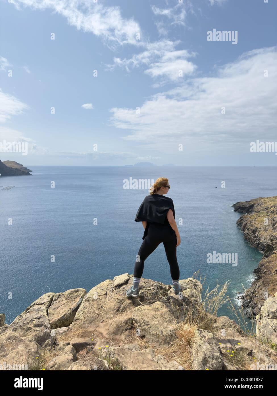Tourist stands on edge of a cliff on rocky coast of Ponta de Sao Lourenco, Madeira Island. Surrounded by waves and towering rocks, they embrace the fr - Smartphone Captured Stock Image