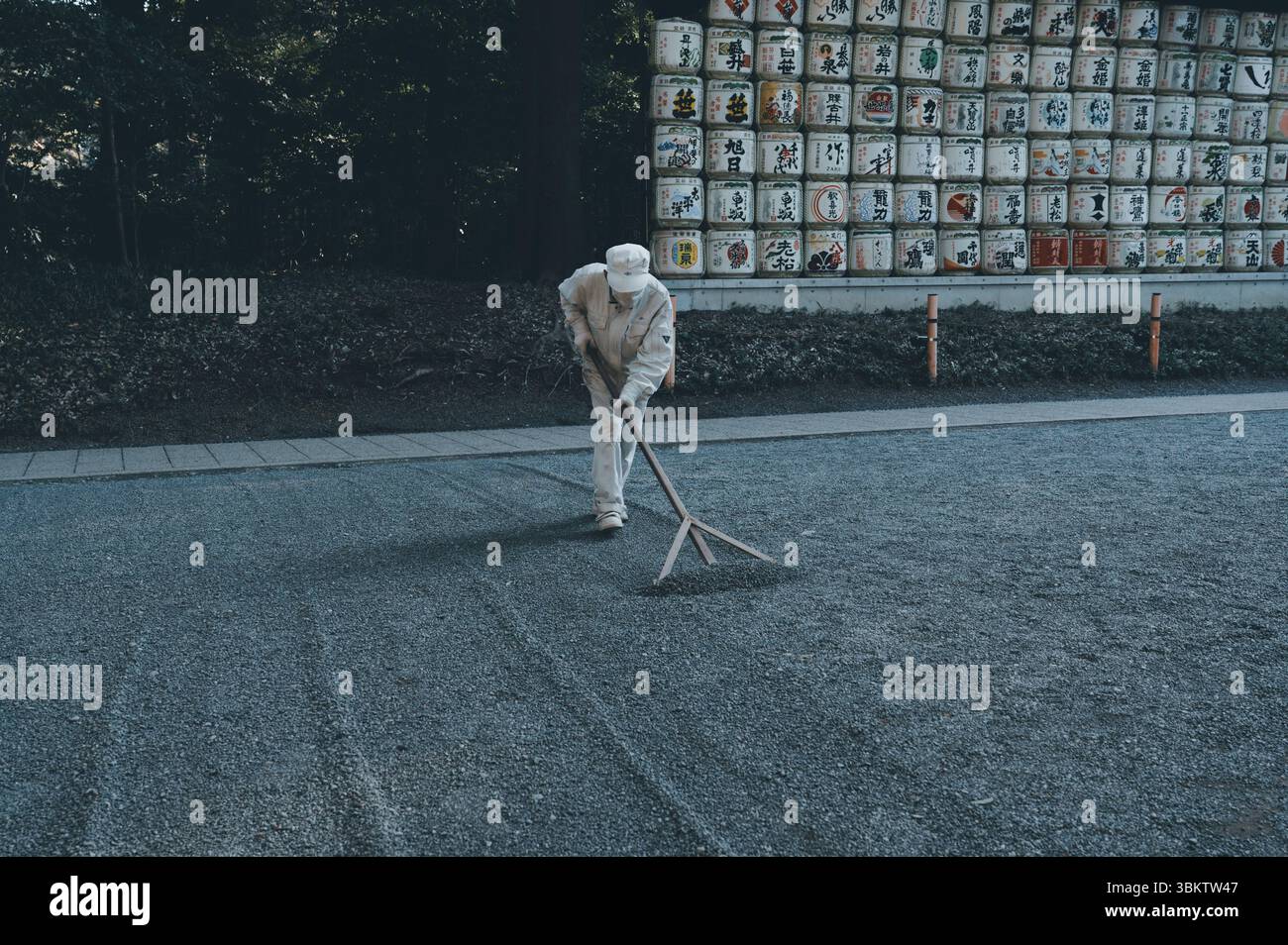 Shrine worker purposefuly rakes a gravel path at Meiji Jingu Shrine ...