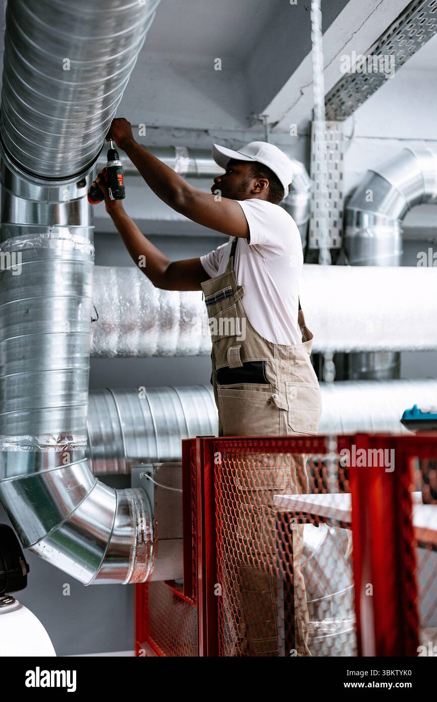 Skilled worker installing ventilation pipes in modern facility during daylight hours Stock Photo