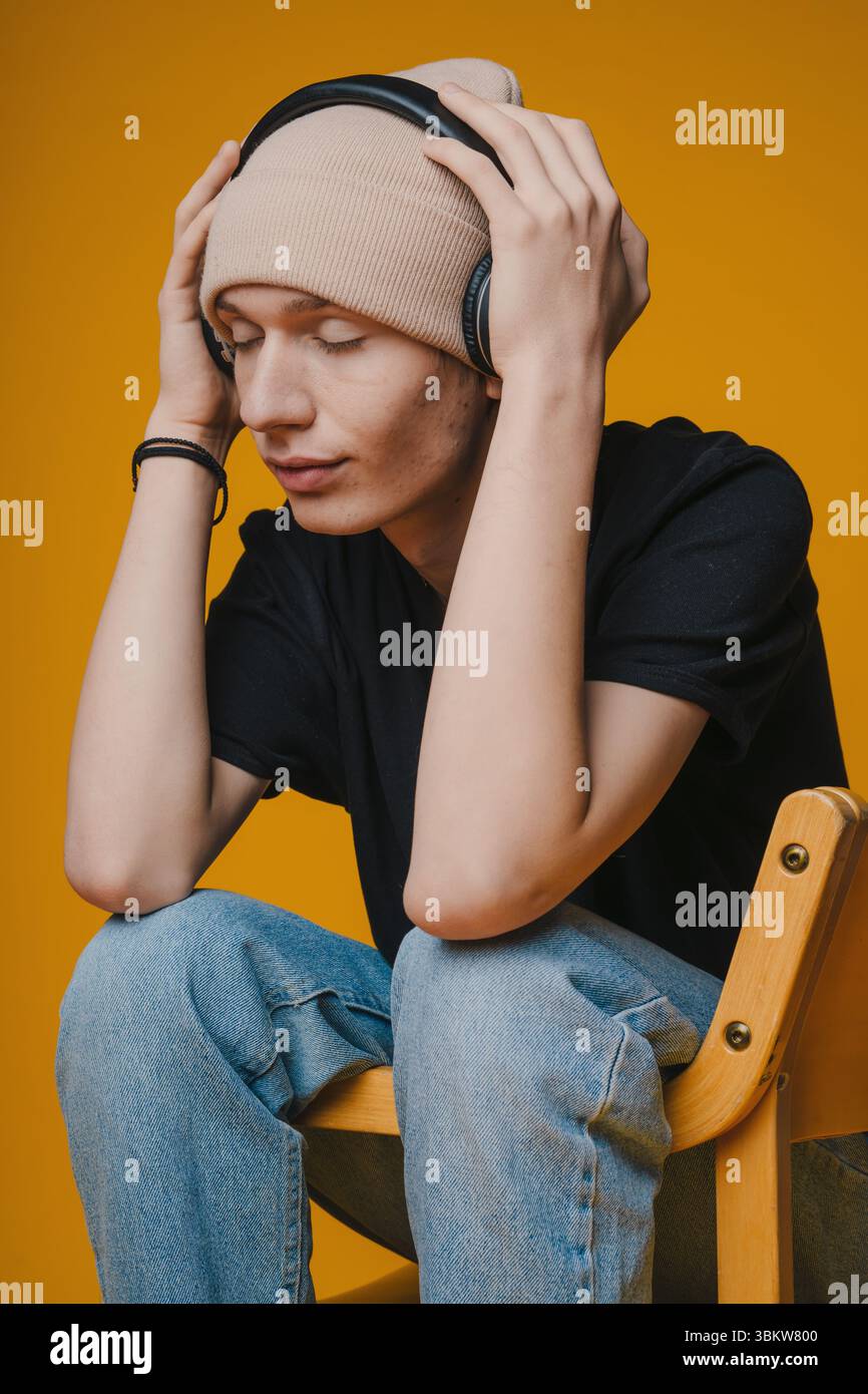 A young person wearing headphones, sitting with closed eyes, deeply immersed in music Stock Photo