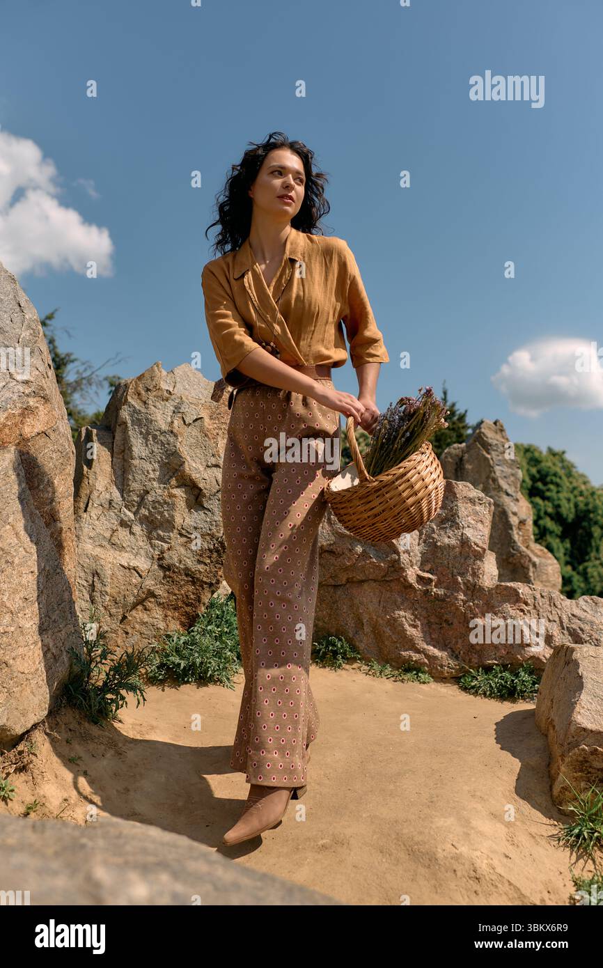 A young woman with curly hair poses by scenic rocks, flaunting her ...
