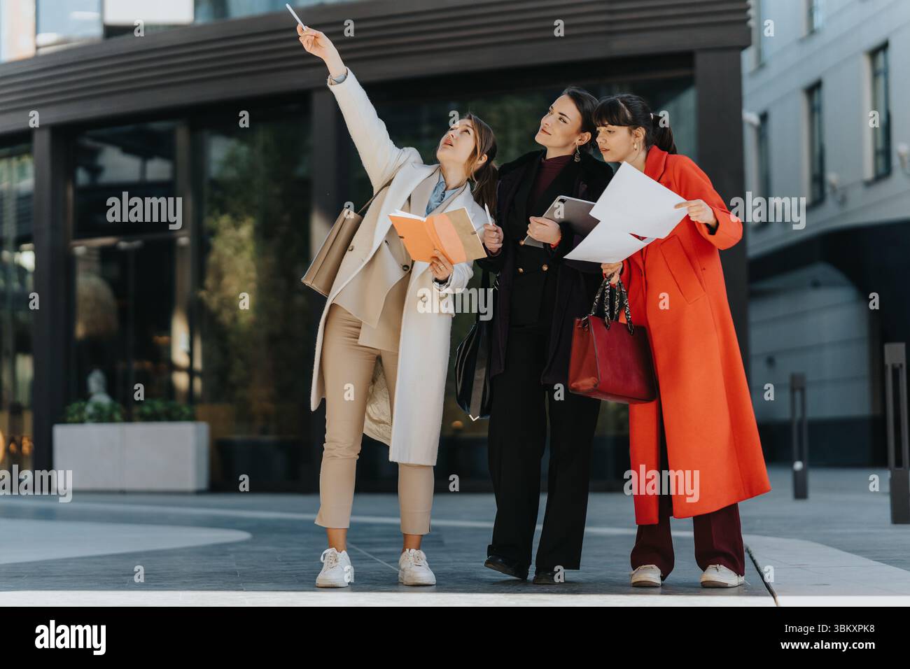 Three female professionals discuss plans outdoors with documents Stock Photo