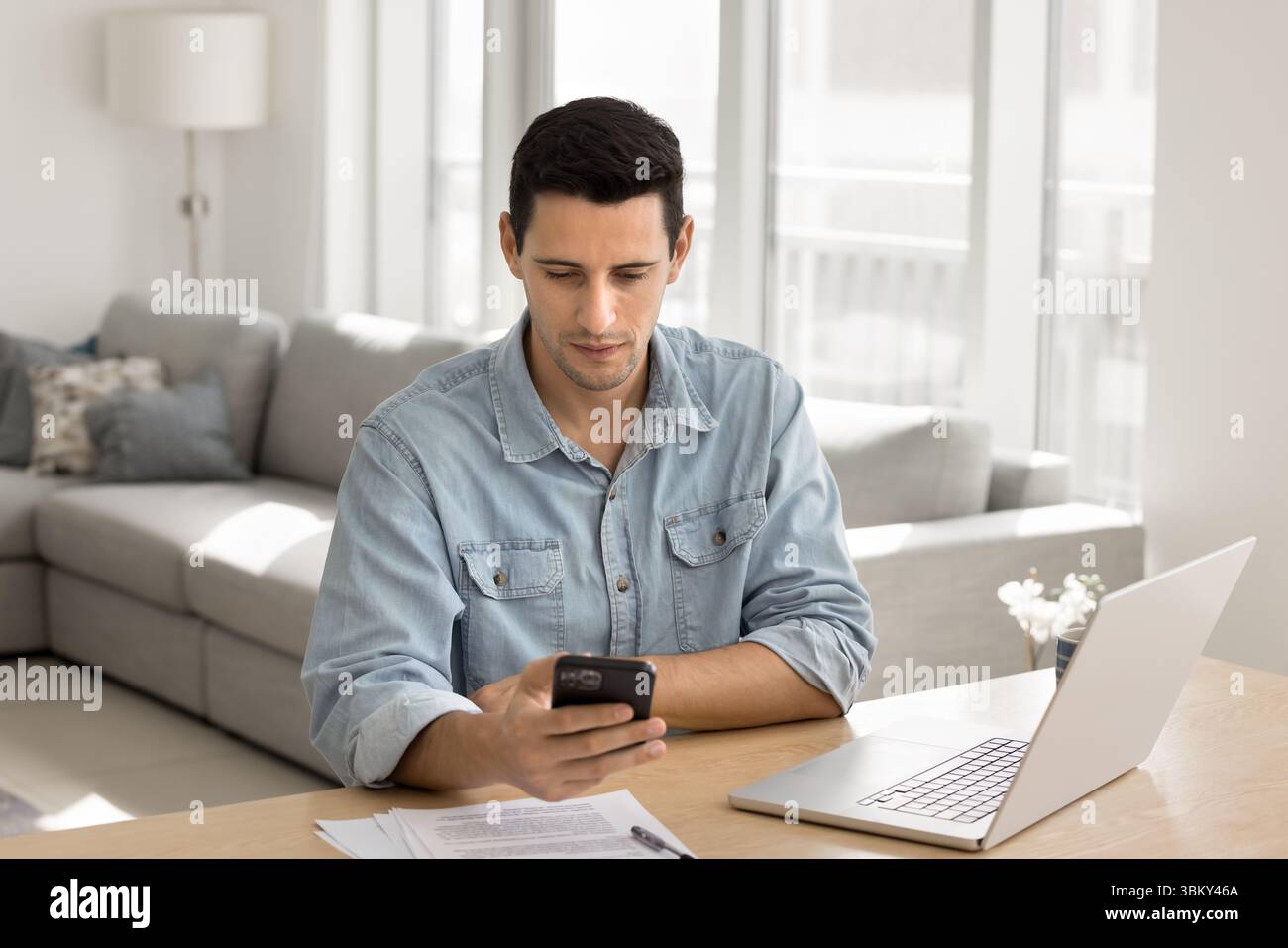 Focused young male remote working professional multitasking using phone notebook Stock Photo