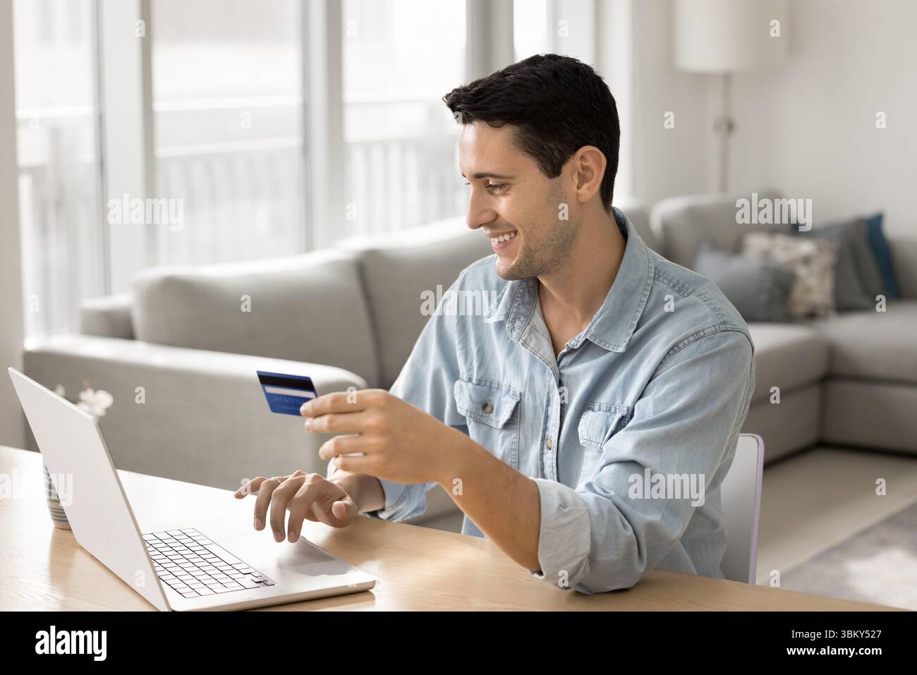 Smiling young man pay online from credit card using notebook Stock Photo