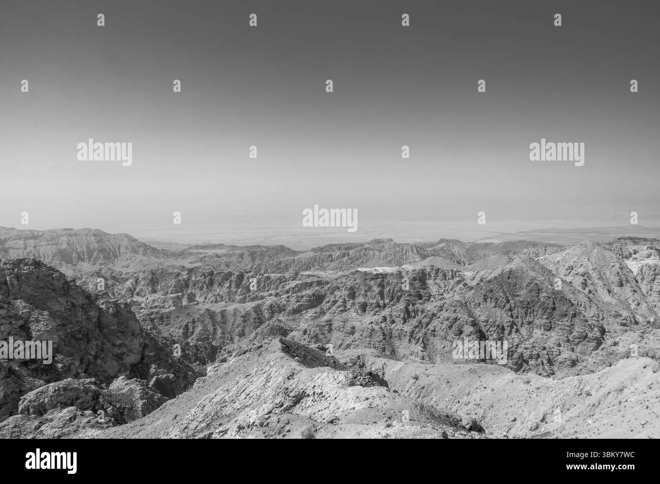 A black and white photo of a mountain range with a clear blue sky. The mountains are rocky and barren, with no vegetation in sight. The sky is a deep Stock Photo