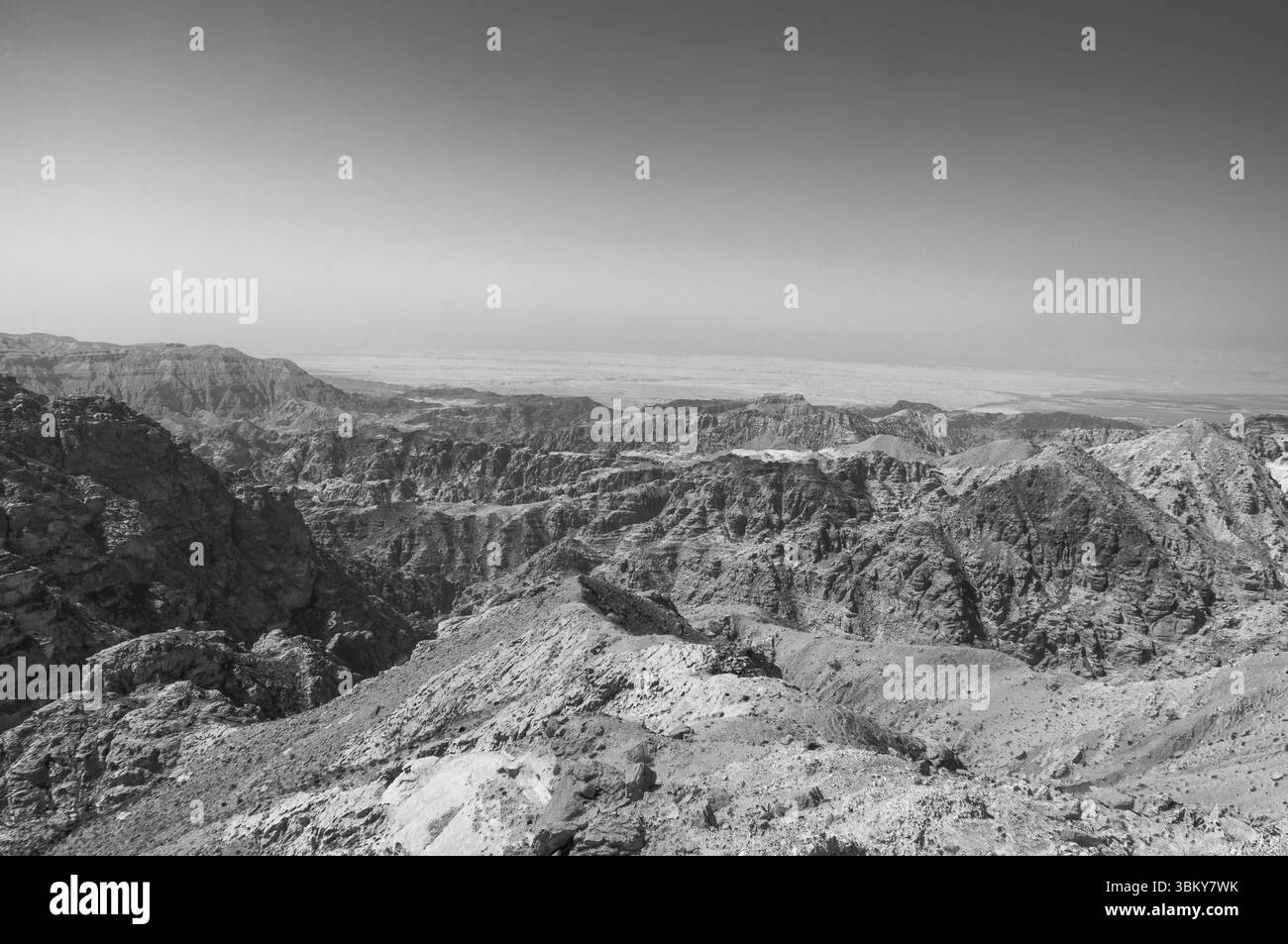 A black and white photo of a mountain range with a clear blue sky. The mountains are rocky and barren, with no vegetation in sight. The sky is a deep Stock Photo